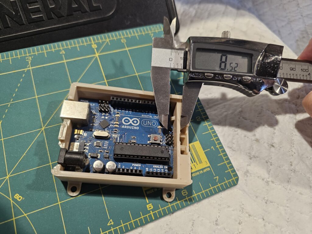 General Tools Digital Caliper measuring the distance between components on an Arduino Uno board inside a 3D printed enclosure